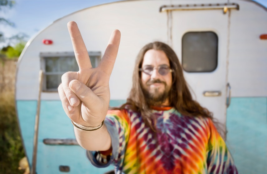 Hippie staat voor caravan en maakt het vredesteken.